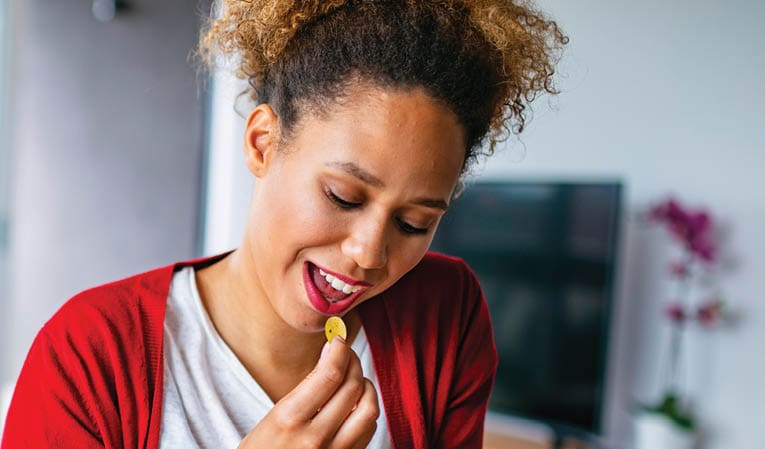 Cheerful mixed race woman taking vitamin pills in order to improve her health